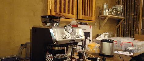 A coffee machine on a wooden table in a kitchen with bamboo walls and shelves.