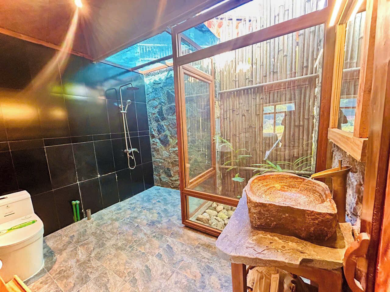 A bathroom with a stone sink, a shower, and a view of a bamboo fence.