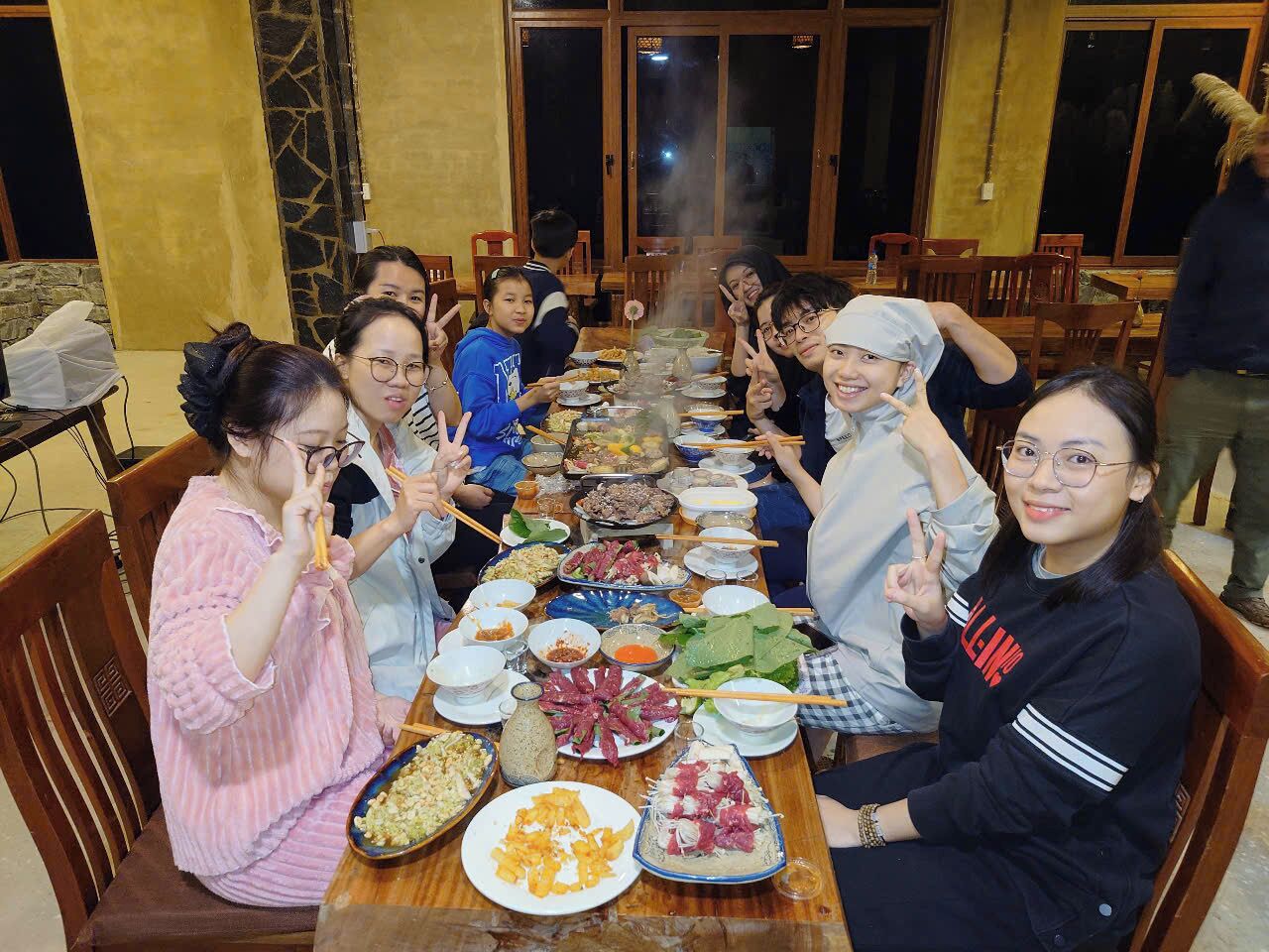 A group of people seated around a long table with various dishes, indicating a communal dining setting.