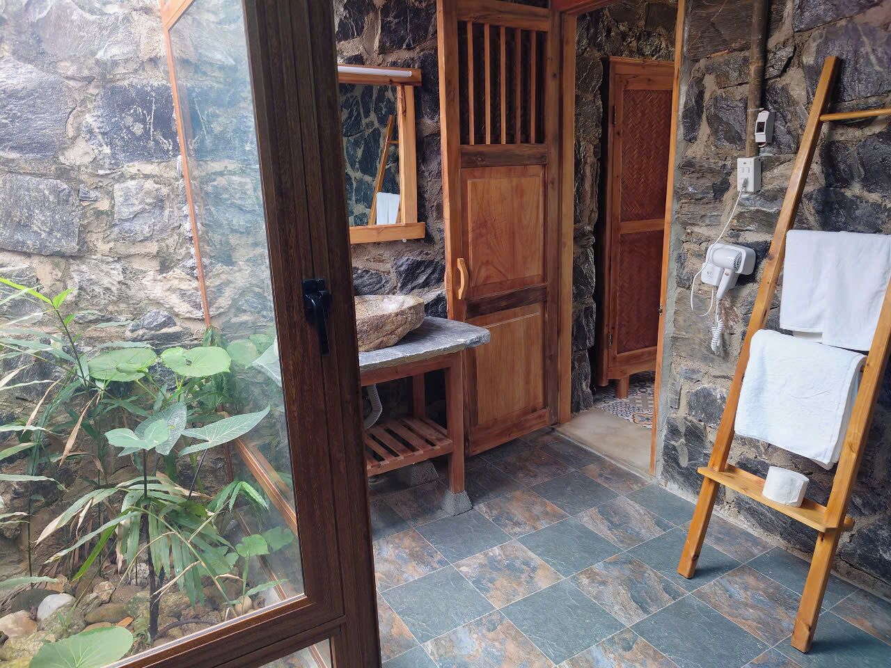 A rustic bathroom with a stone wall, wooden door, and a wooden drying rack.
