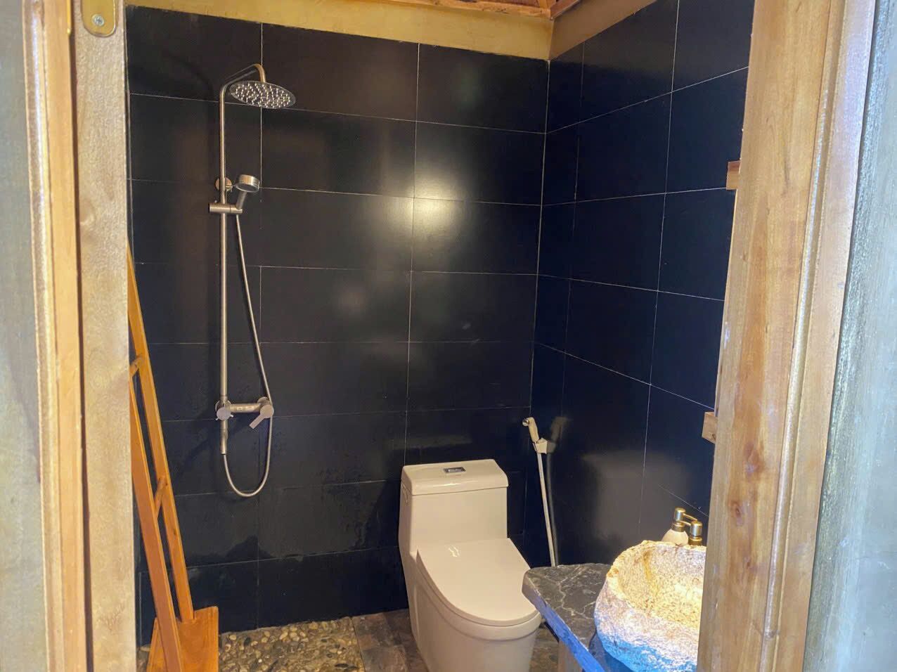 Een kleine badkamer met donkere tegels, een toilet, een douche en een wastafel.