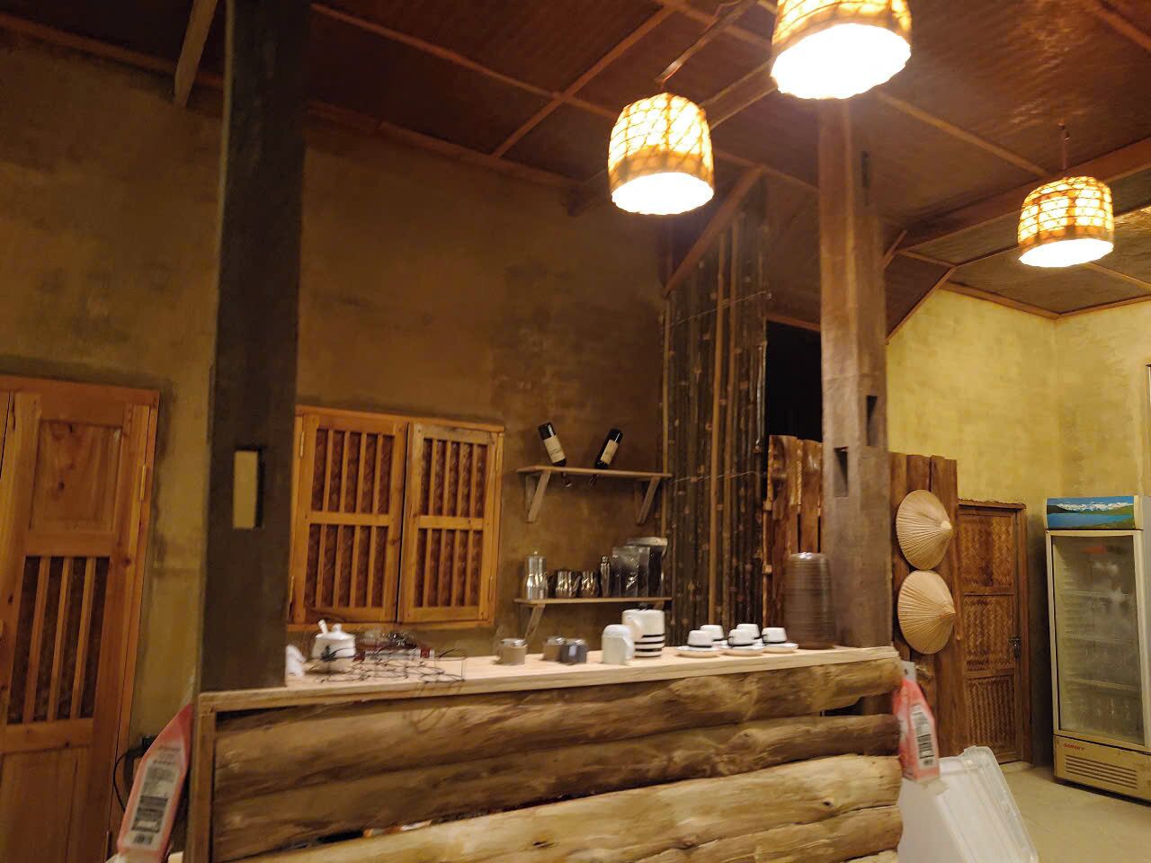 A rustic interior with wooden beams, a counter with various items, and hanging lamps.