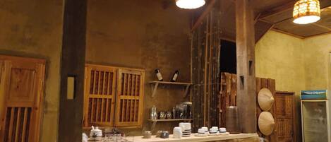 A rustic interior with wooden beams, a counter with various items, and hanging lamps.