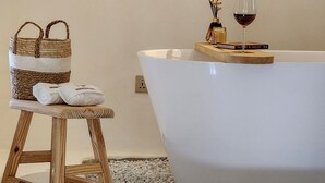 A modern bathroom with a freestanding bathtub, a wooden stool, and a wicker basket. - Luxury 2BHK Escape w/ Hot Tub, Free Wi-Fi, AC (Kathmandu)