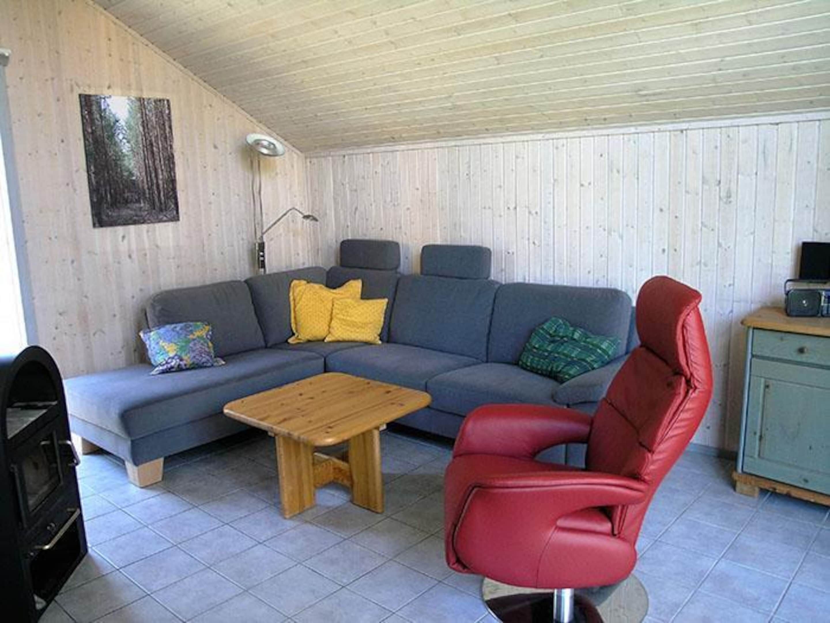 Un salon comprenant un canapé d’angle, un fauteuil rouge, une table basse en bois et un petit meuble.