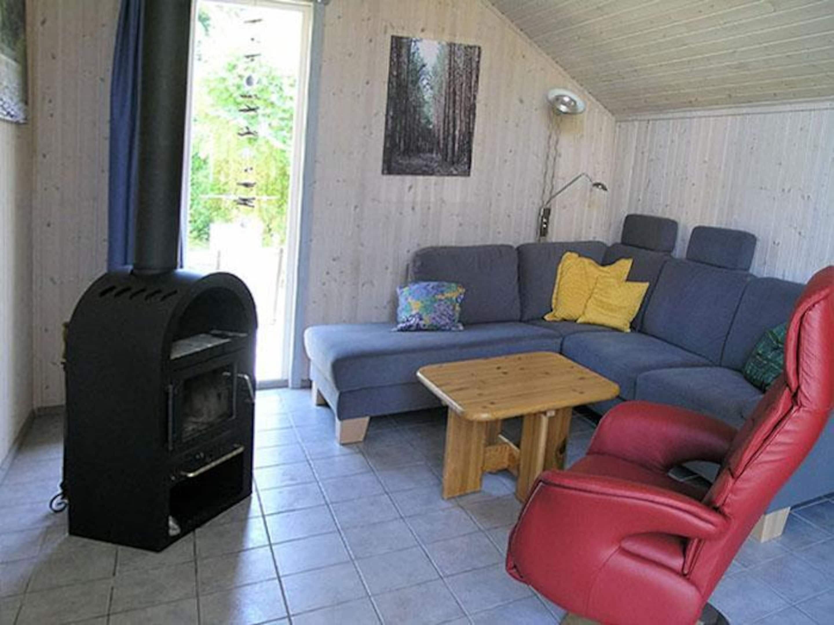 A living room with a sofa, a red chair, a small wooden table, and a wood-burning stove.