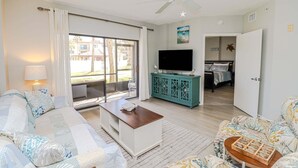 Una sala de estar con sofá, mesa de centro, televisor y vistas al exterior por una puerta corrediza.