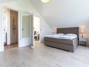 A bedroom with a bed, bedside tables, a nightstand, a lamp, and a shower area. - Doppelhaushalfte Direkt am Hafen von Tonning (Toenning)