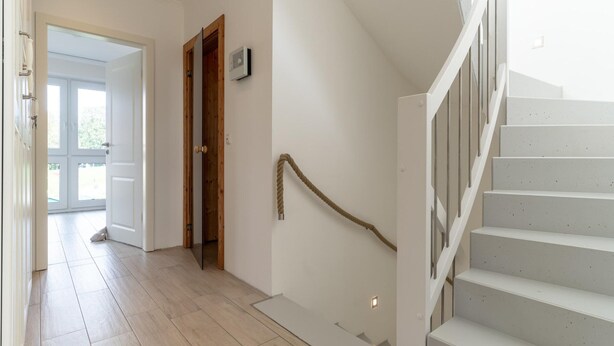 Una escalera con barandilla y una puerta de madera que da a otra habitación.
