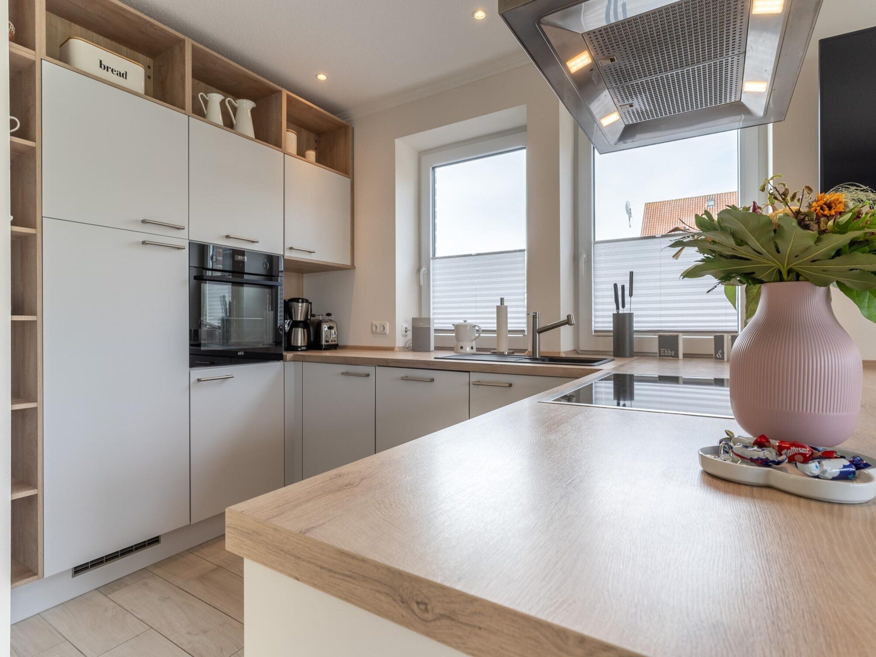 A modern kitchen with white cabinetry, a built-in oven, a coffee maker, and a vase with flowers on the counter.