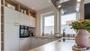 Una cocina moderna con gabinetes blancos, horno empotrado, cafetera y un florero con flores en la encimera.
