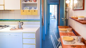 A kitchen with a dishwasher, a stove, and a coffee maker. There is a dining table with plates, cups, and cutlery. The kitchen has blue walls and yellow cabinets. - Wiew Acitrezza (Acicastello)