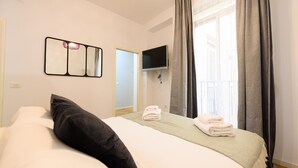 A hotel room with a bed, a flat-screen TV mounted on the wall, and a window with curtains.