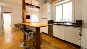 A modern kitchen with a wooden bar stool, a dishwasher, and a window with a view of greenery.