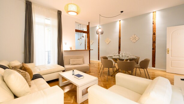 A modern living room with white sofas, a dining table with chairs, and a wooden floor.