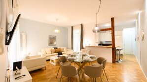 A modern living room with a glass dining table, beige sofas, and a wooden floor.