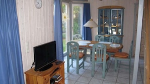 A dining area with a wooden table and chairs, a television on a wooden stand, and a cabinet with glass doors. - Ferienhaus im Ferienpark Mirow (Mirow)