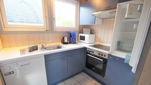 A compact kitchen with a dishwasher, microwave, stove, and sink. - Ferienhaus im Ferienpark Mirow (Mirow)