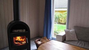 A room with a wood-burning stove, a sofa, and a window with a view of greenery. - Ferienhaus im Ferienpark Mirow (Mirow)