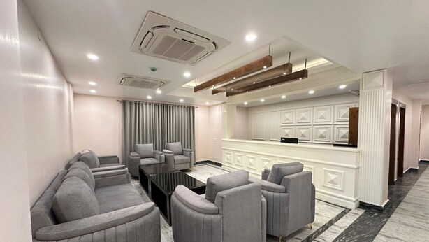A modern living room with grey sofas, a coffee table, and a kitchen area with white cabinetry and a countertop. - LUXE HAVEN RESIDENCY (Budgam)