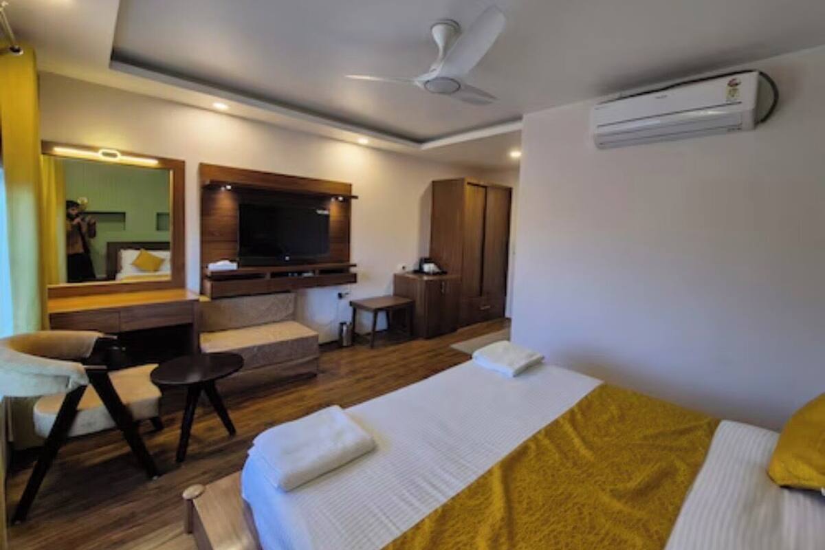 A hotel room with a bed, a TV, a ceiling fan, and an air conditioning unit.