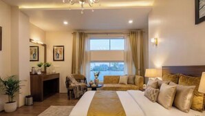 A hotel room with a large bed, a desk, a chair, a sofa, and a view of the outdoors. - LUXE HAVEN RESIDENCY (Budgam)