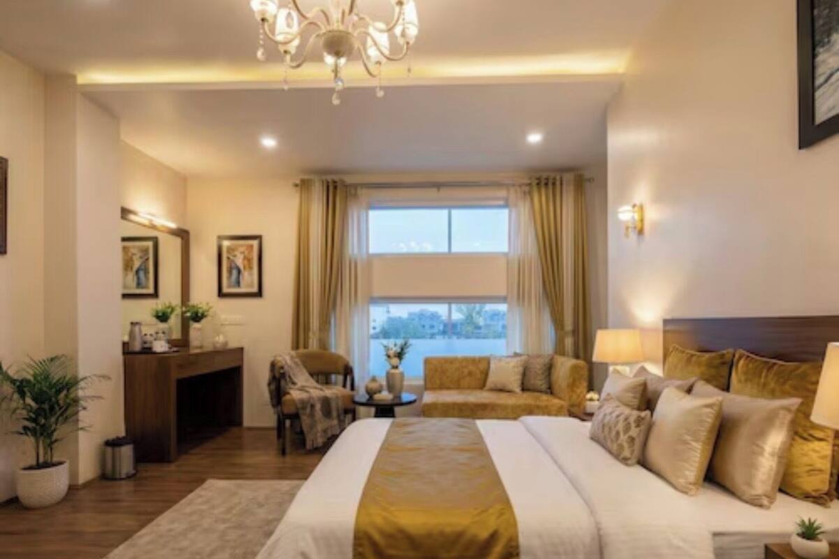 A hotel room with a large bed, a desk, a chair, a sofa, and a view of the outdoors.