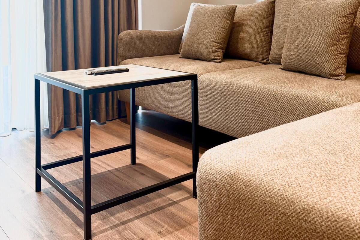 Uma sala de estar moderna com um sofá, uma mesa pequena e uma janela com cortinas.