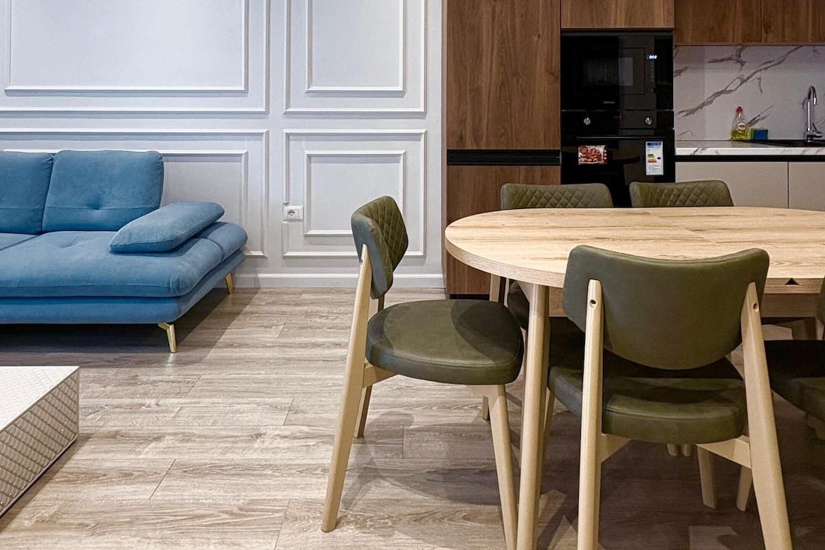 Uma sala de estar moderna com um sofá azul, uma mesa de jantar de madeira e cadeiras.