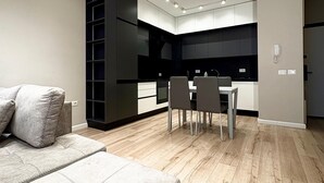 A modern living room with a sofa and a dining area with chairs and a table. There is a kitchen area with cabinets and a countertop. - Blue Boutique Apartments 1 (Farke)