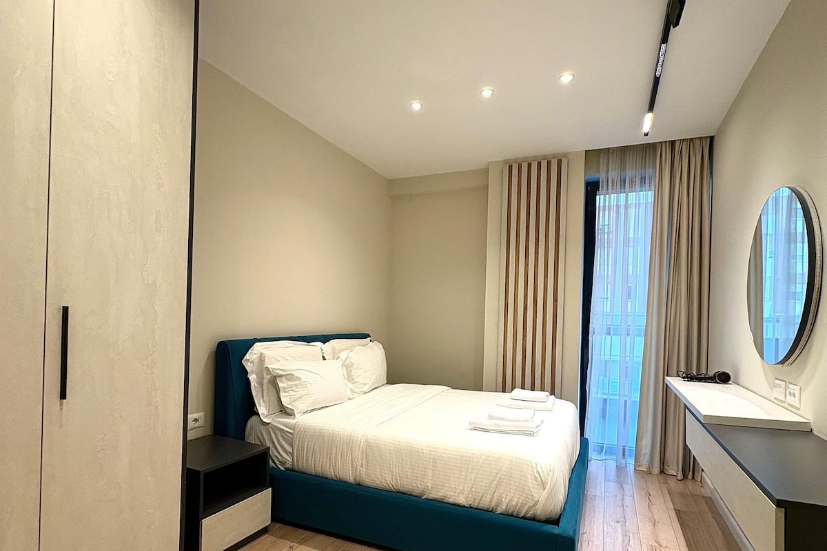 Quarto moderno com cama grande, guarda-roupa, mesa de cabeceira e banheiro com espelho.