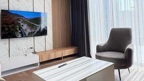 A modern living room with a flat-screen TV mounted on a marble wall, a white coffee table, a grey armchair, and a black ceiling light fixture. - Blue Boutique Apartments 1 (Farke)