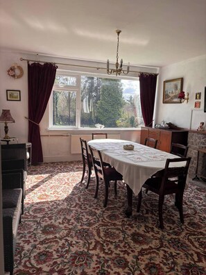 A dining room with a table set for four, a chandelier, and a view of trees through the window. - Luxurious Meath Retreat With 5 Bedrooms (Oldcastle)