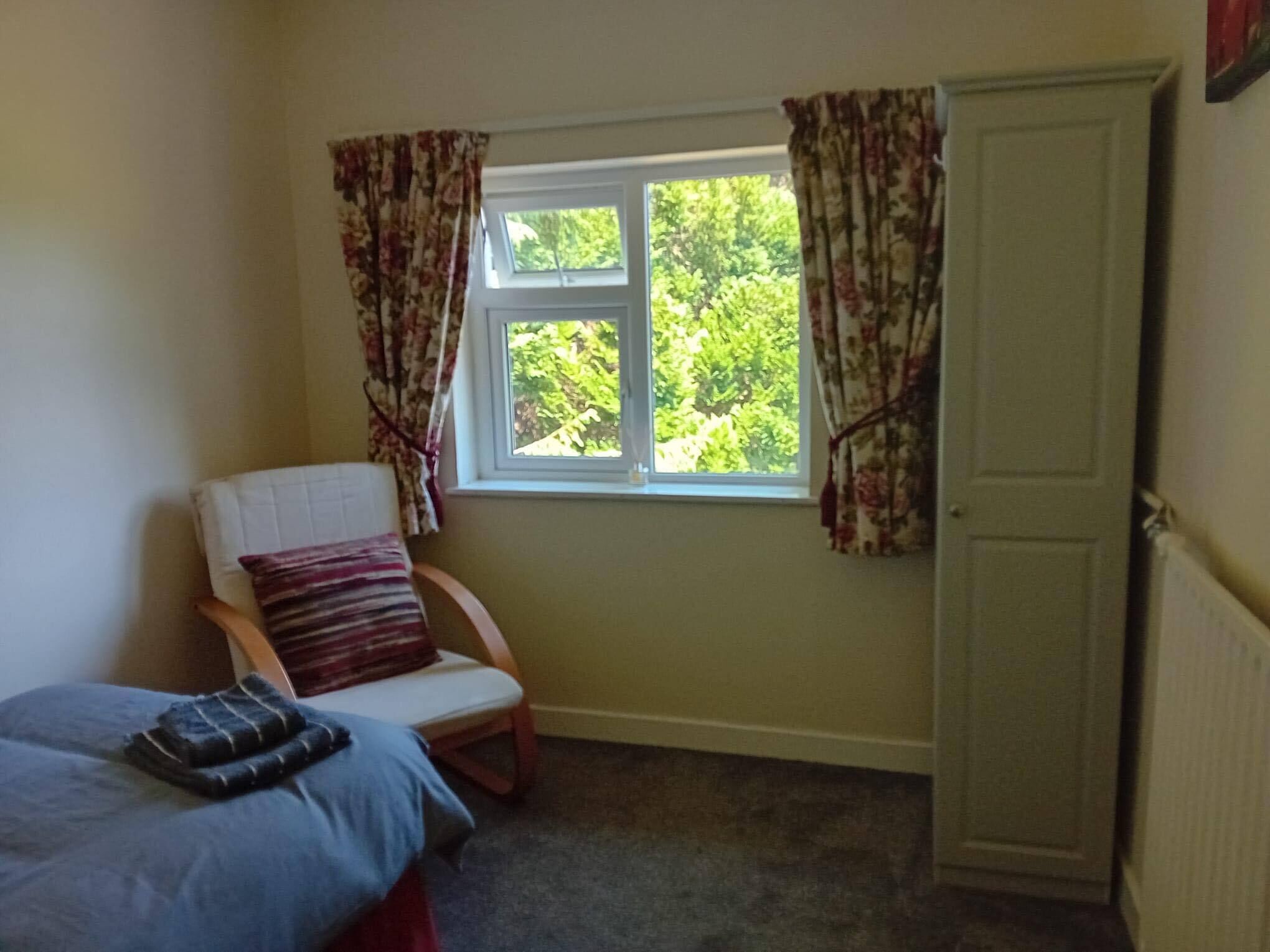 A bedroom with a bed, a chair, a window with curtains, and a door.