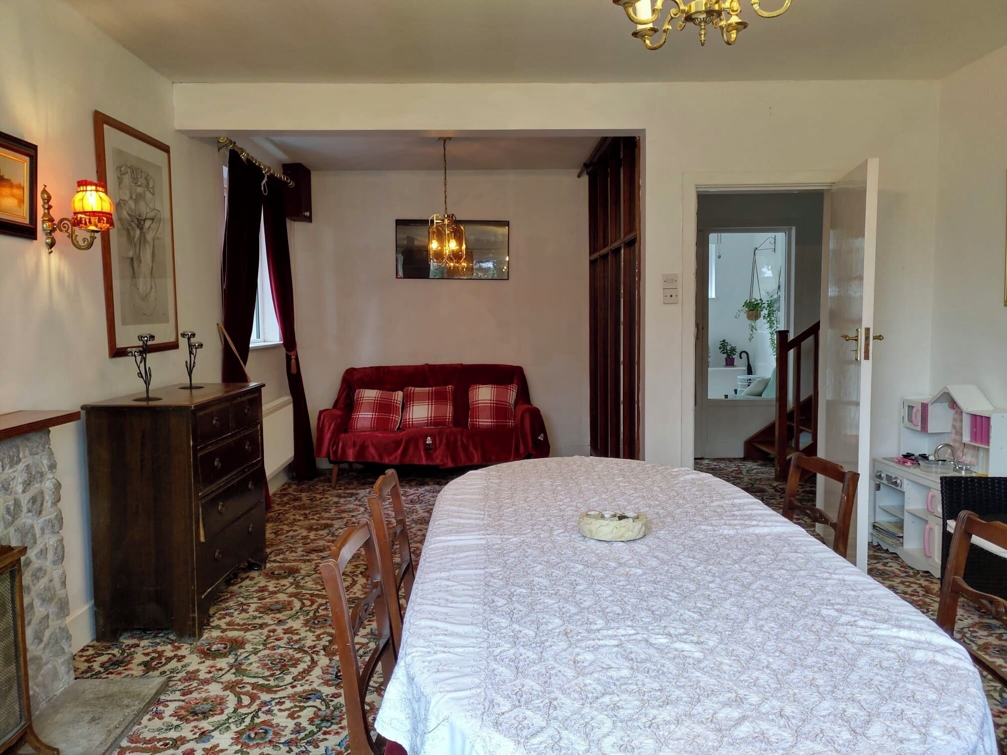 A cozy bedroom with a large bed, a red sofa, a wooden dresser, and a chandelier.