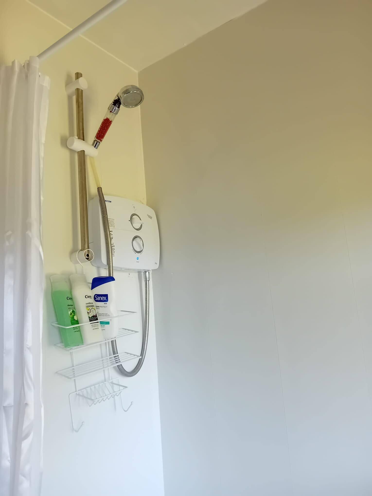 A shower area with a handheld showerhead, a wall-mounted faucet, and a shower control panel. There are toiletries on a shelf below the shower.