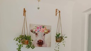 A room with a light green armchair, a small white side table with a book, and two hanging planters with green plants.