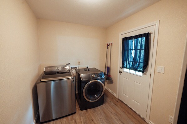 Une buanderie équipée d’un lave-linge et d’un sèche-linge, d’un balai et d’une porte avec une fenêtre.