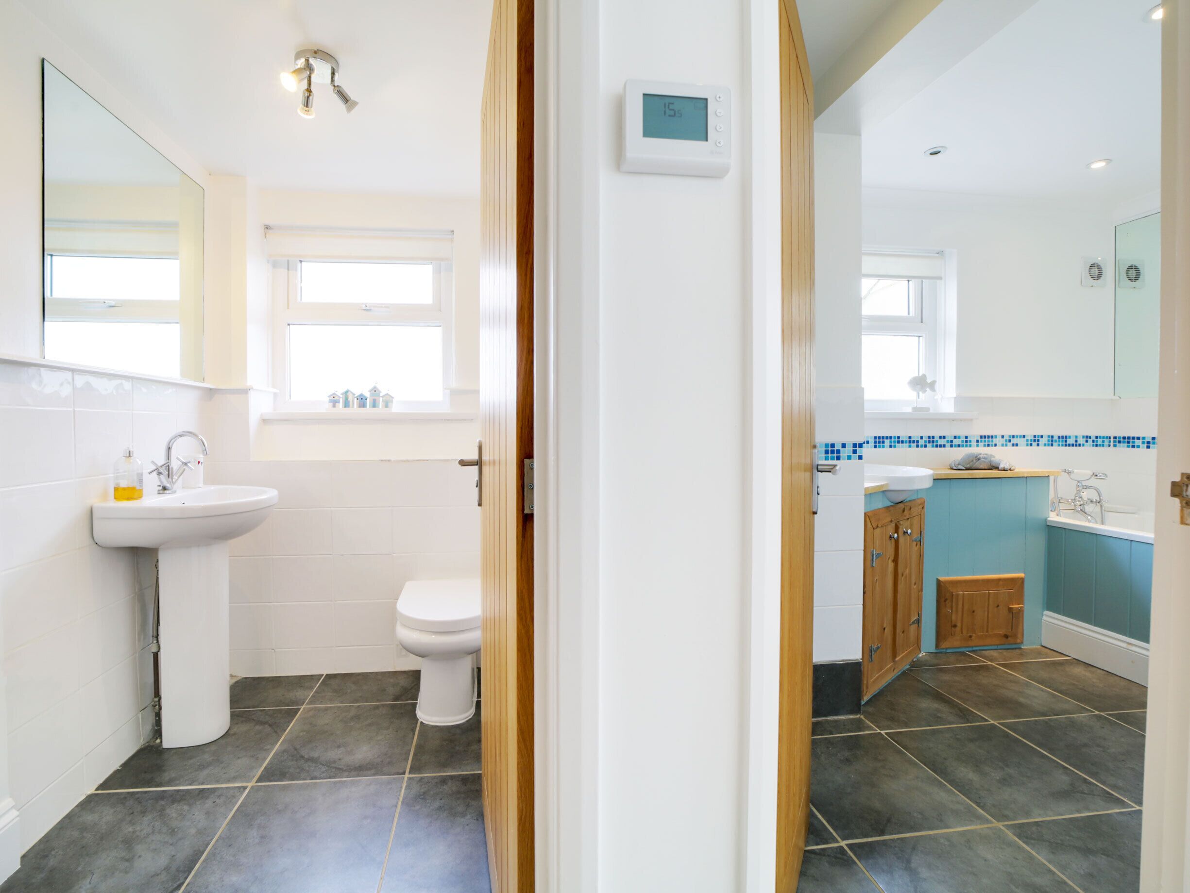 Een moderne badkamer met een wit wastafelmeubel, toilet en een douchegedeelte betegeld met blauwe tegels.