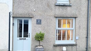 Edifici de dues plantes amb una porta blanca i una finestra amb persianes. Un petit plantà en test és col·locat al costat de la porta.