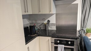 A modern kitchen with white cabinets, a black countertop, stainless steel appliances, and a small window with curtains. - Cosy Coastal Apartment in Lytham St Anne's (Lytham St. Anne's)