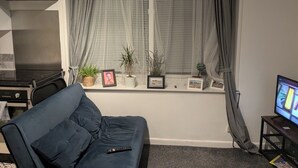 A living room with a sofa, a TV, and a window with curtains. - Cosy Coastal Apartment in Lytham St Anne's (Lytham St. Anne's)
