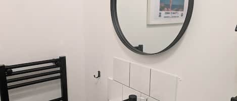 Une salle de bain avec un lavabo blanc, un robinet noir et un miroir rond orné d’un cadre contenant une image.