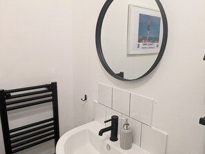 A bathroom with a white sink, black faucet, and a round mirror with a framed picture. - Cosy Coastal Apartment in Lytham St Anne's (Lytham St. Anne's)