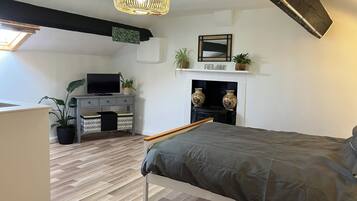 A bedroom with a bed, a TV on a dresser, a fireplace, and a ceiling light.