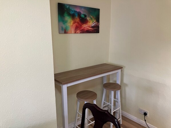 A small kitchenette with a wooden countertop, two stools, and a colorful abstract painting on the wall.