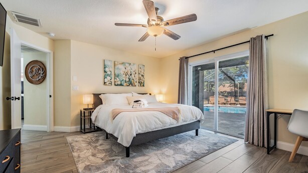 Une chambre avec un lit, un ventilateur de plafond, une grande fenêtre et une vue sur une piscine.