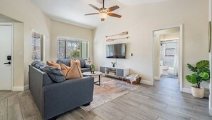 Un salon moderne avec un canapé gris, un téléviseur à écran plat et un ventilateur de plafond.