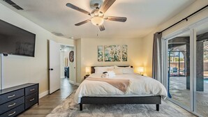 Une chambre à coucher comprenant un lit, des lampes de chevet, un ventilateur de plafond, un téléviseur et une porte-fenêtre coulissante donnant sur une terrasse.