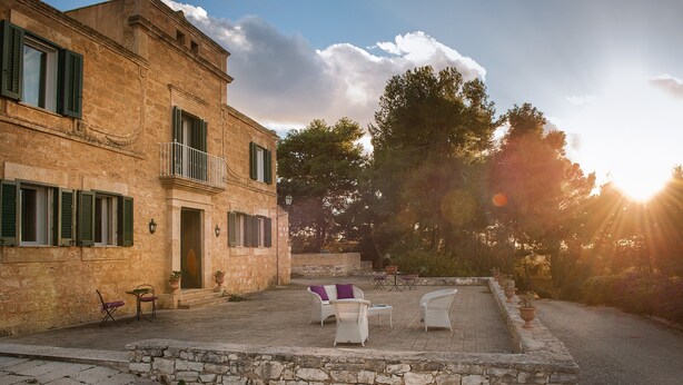 Un edificio de piedra con un patio, mesas al aire libre y vistas a árboles y al cielo.
